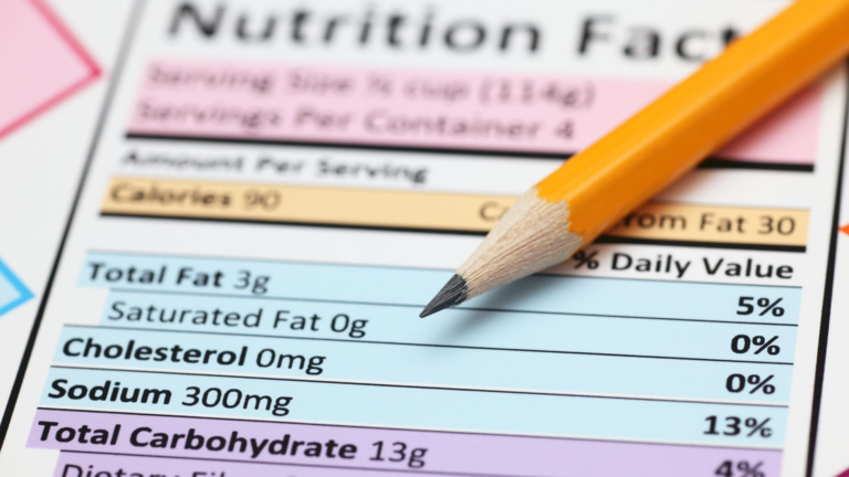 Close-up of a sharpened yellow pencil pointing at the nutrition facts label, highlighting sodium and cholesterol information on a food package, with nutrition terms explained for better understanding.